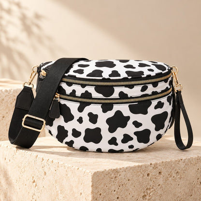 ZOCOIFY Everyday Roomy Crossbody Bag in cow print styled on a pale stone plinth